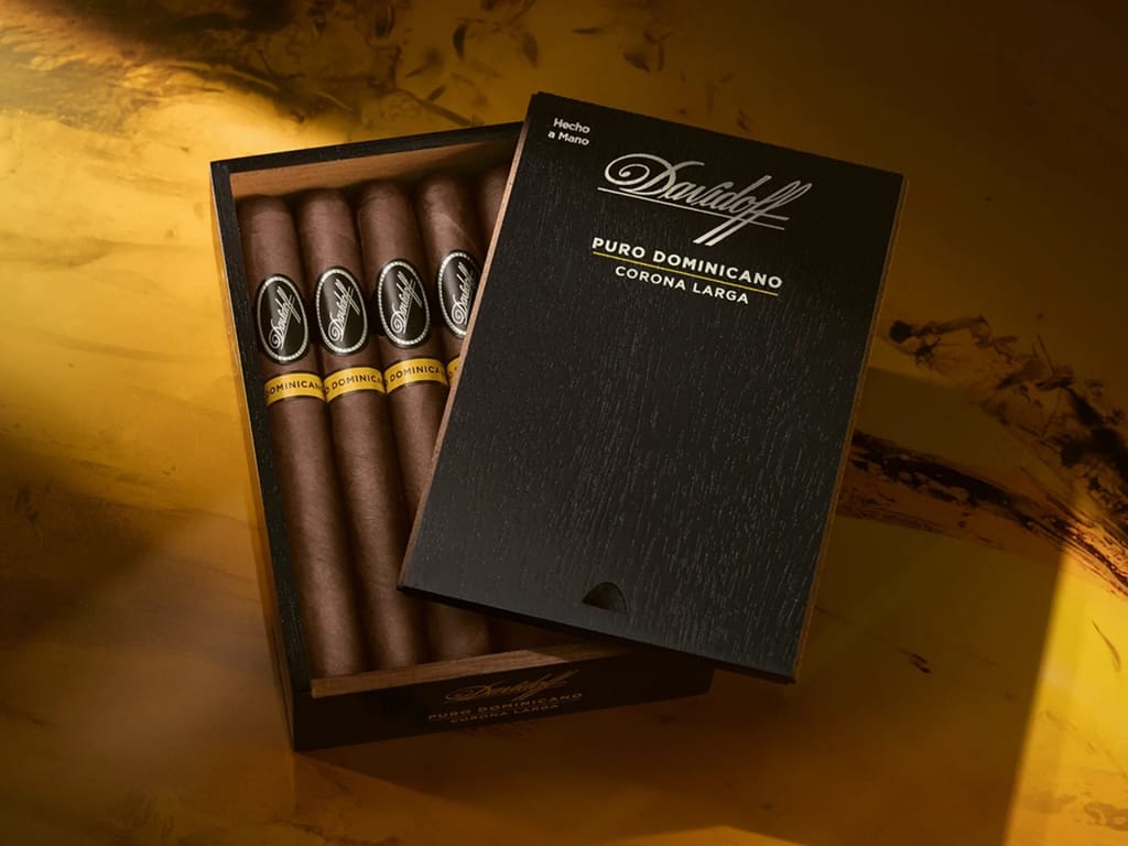 An open wooden box labeled "Davidoff Puro Dominicano Corona Larga" reveals neatly arranged cigars against a warm golden-brown background.