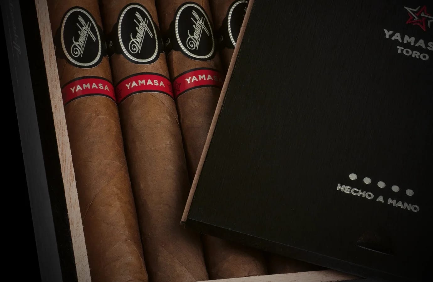 Close-up of Davidoff Yamasa Toro cigars in a black wooden box, showing brown wrappers, red bands, and elegant premium packaging with lid partly open.